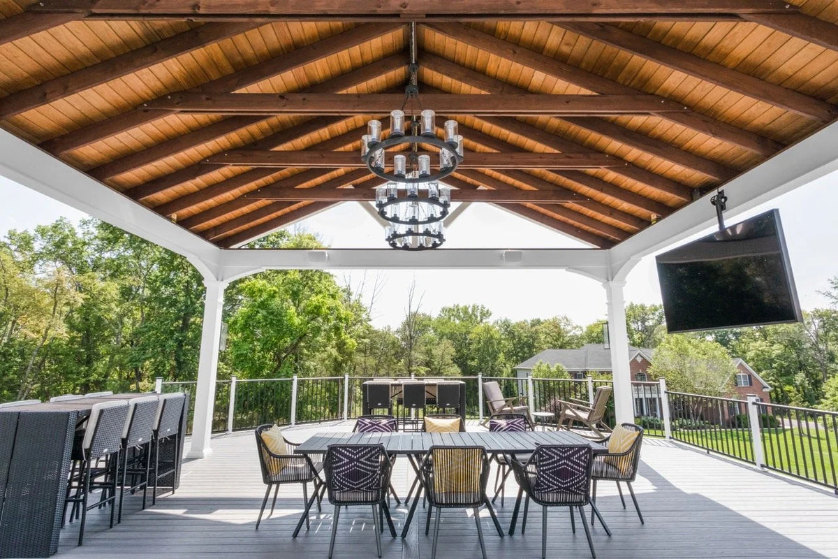 Creative Gazebos Manor A-Frame Vinyl Pavilion: An outdoor covered patio with a wooden ceiling, a chandelier, a dining table with chairs, and a large flat-screen TV mounted on the ceiling. Manufacturer family example; size, finishes and optional features vary.