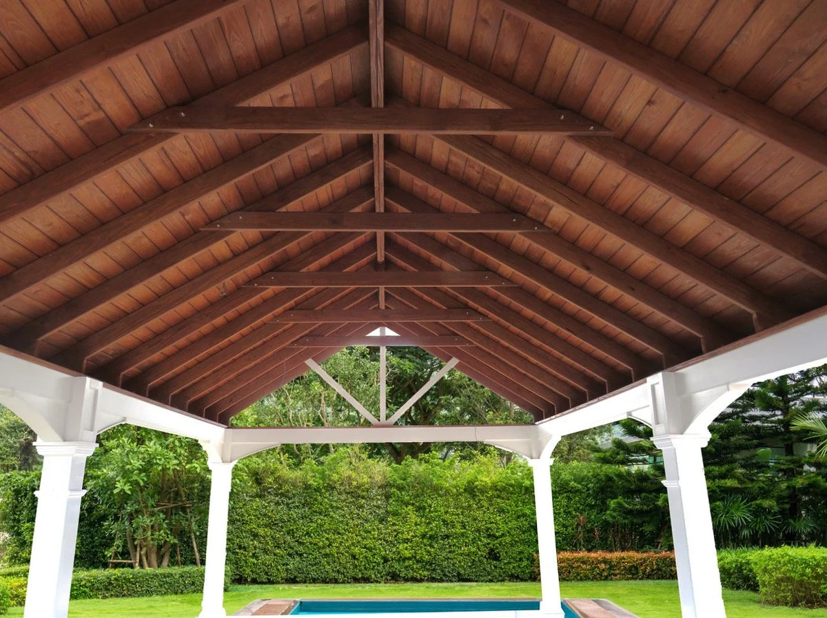Creative Gazebos Manor A-Frame Vinyl Pavilion: View of a covered outdoor patio with a wooden roof and white columns, overlooking a backyard with green grass, bushes, and trees. Manufacturer family example; size, finishes and optional features vary.